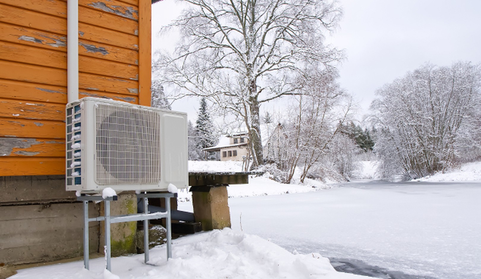 A heat pump next to an old house near a snowy field